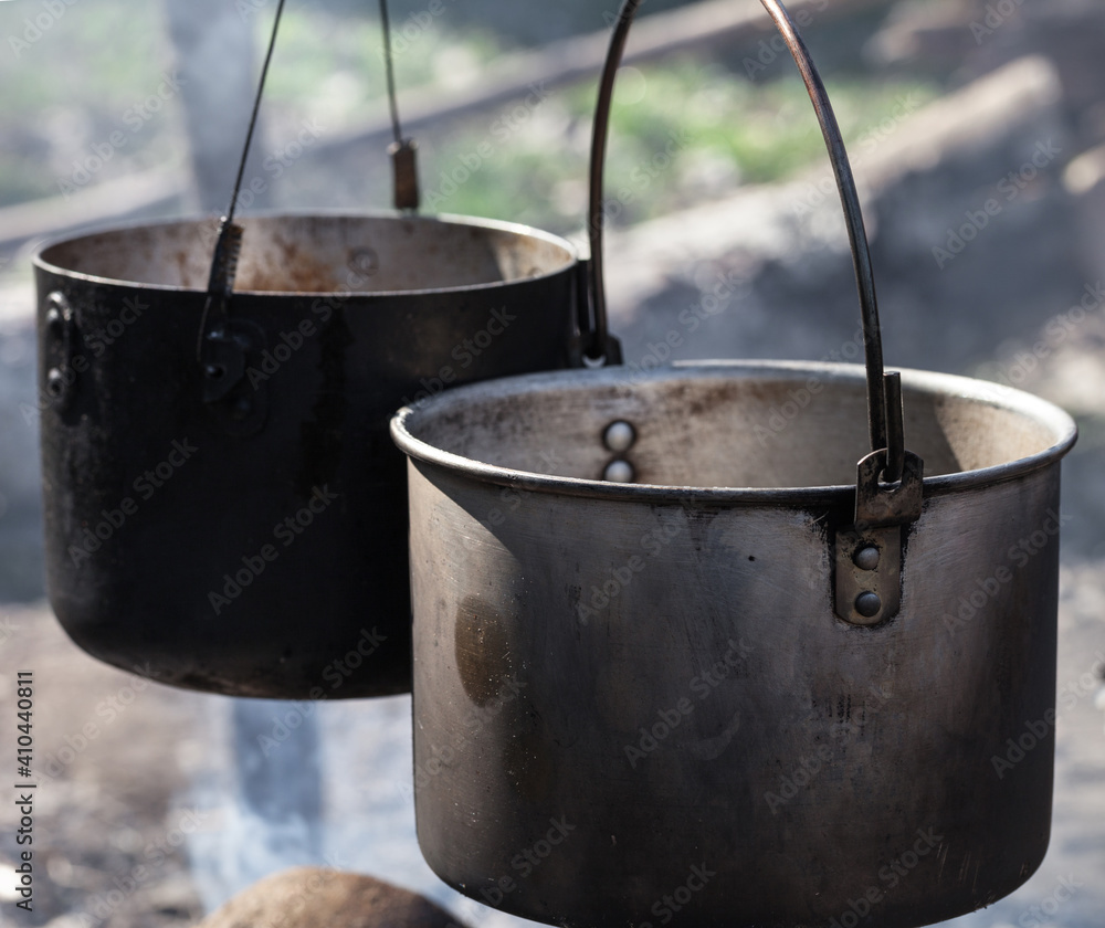 Cooking in two sooty old cauldrons on campfire at sunny day Cooking in two sooty old cauldrons on campfire at sunny day