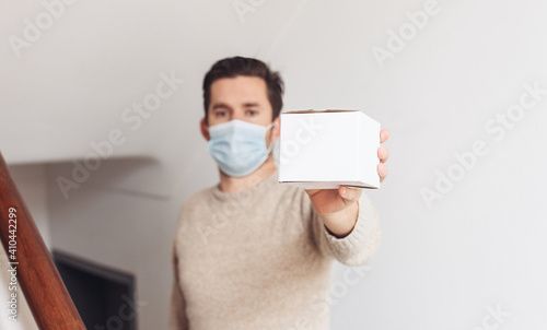A man in medical mask holding and giving a white box to a customer 