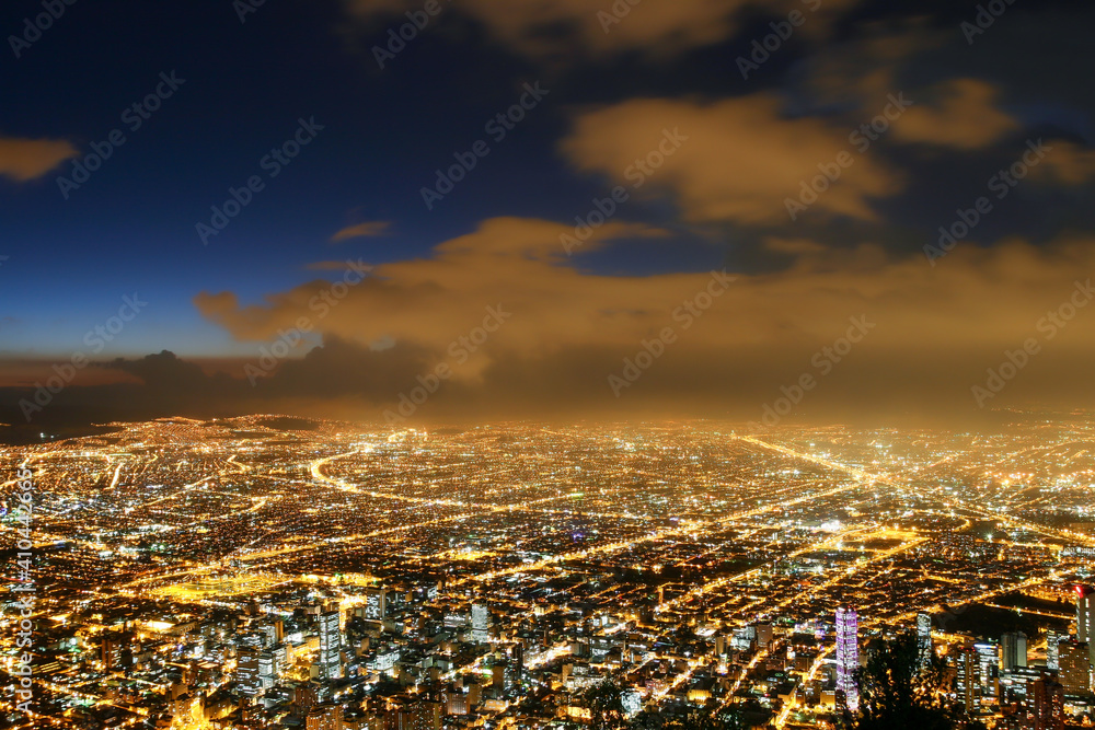 Fototapeta premium Beautiful aerial view of Bogota city at night with business buildings, street lights, avenues and sky at dusk with clouds in the background. Selective focus. Concept of travel, tourism, vacation.