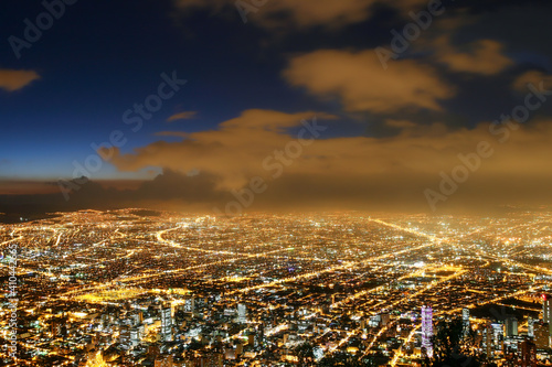 Beautiful aerial view of Bogota city at night with business buildings, street lights, avenues and sky at dusk with clouds in the background. Selective focus. Concept of travel, tourism, vacation.