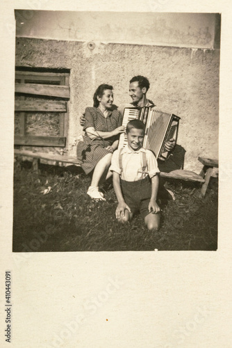 Latvia - CIRCA 1930s: A family shot of married couple with a child in porch outdoor. Man with accordions.Vintage art deco era photo
