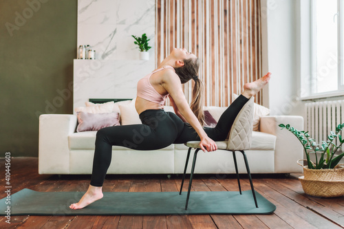 Young fit flexible woman wearing sportswear do stretching exercises in living room. Indoors workout. Training at home.