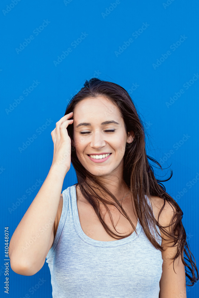Portrait of a beautiful young woman smiling and playing with her hair and the wind with a blue background Portrait of a beautiful young woman smiling and playing with her hair and the wind with a blue background