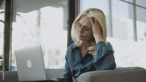 Tired stressed upset middle aged mature woman feeling sick headache after computer work sit on sofa, sad fatigued senior lady grandmother touching head suffering from ache pain migraine