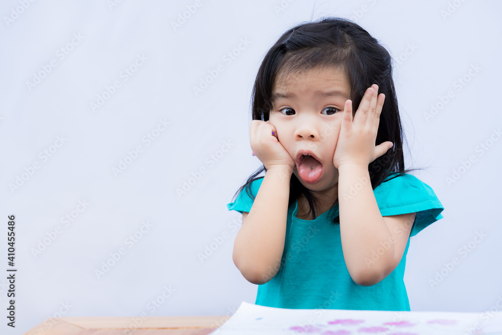 Cute girl showed angry expression. Child squeezes her cheek with both hands. Children sticks out his tongue, frustrating with homework when the school is closed and is stay at home. Kid study hard. Cute girl showed angry expression. Child squeezes her cheek with both hands. Children sticks out his tongue, frustrating with homework when the school is closed and is stay at home. Kid study hard.