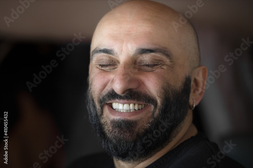 Bearded bald man with beautiful white teeth smiling broadly with closed eyes