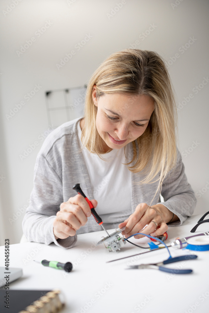 beautiful, blond female electrician sitting at the table in the office fixing a socket and being happy beautiful, blond female electrician sitting at the table in the office fixing a socket and being happy