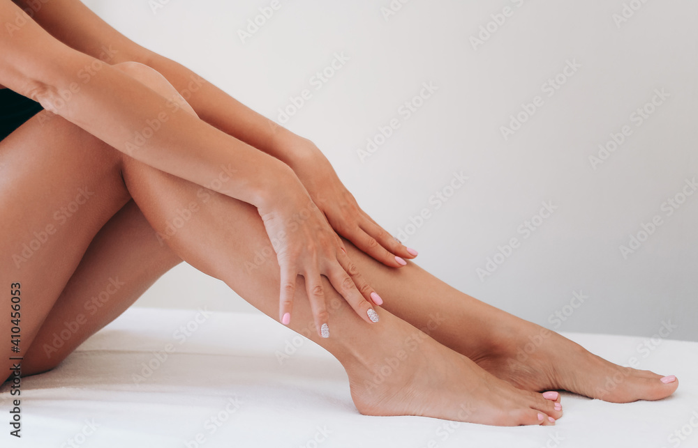 Long woman legs after procedure of epilation on light background. Girl stroking her feet. The concept of spa, epilation, waxing, shugaring, skin care, manicure and pedicure