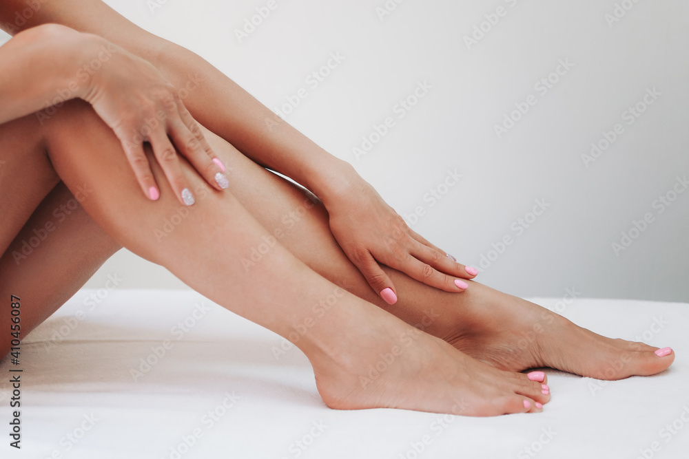 Long woman legs after procedure of epilation on light background. Girl stroking her feet. The concept of spa, epilation, waxing, shugaring, skin care, manicure and pedicure Long woman legs after procedure of epilation on light background. Girl stroking her feet. The concept of spa, epilation, waxing, shugaring, skin care, manicure and pedicure