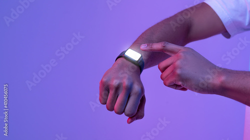 Unrecognizable black man using smartwatch with blank screen in neon lighting, mockup