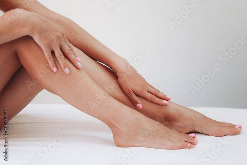 Long woman legs after procedure of epilation on light background. Girl stroking her feet. The concept of spa, epilation, waxing, shugaring, skin care, manicure and pedicure © Ann Marko