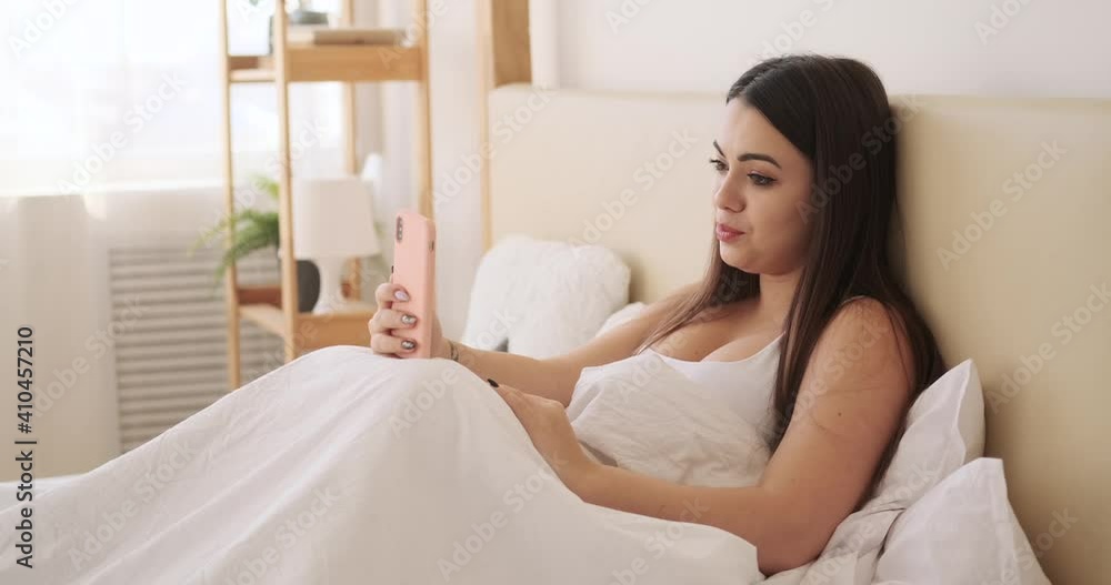 Happy woman video chatting using mobile phone in bed at home