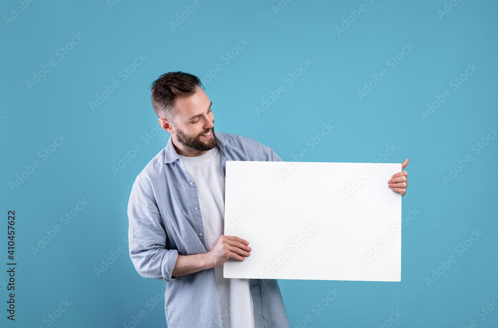 Happy smiling man displaying white blank placard on blue studio background, mockup for logo or design Happy smiling man displaying white blank placard on blue studio background, mockup for logo or design