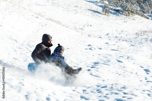 Winter joy and outdoor activity in snowly forest. Father with son enjoying tubing ride on snow hill