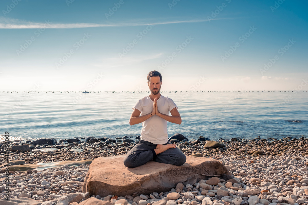 Attractive young man practicing yoga meditation and breathwork outdoors by the sea Attractive young man practicing yoga meditation and breathwork outdoors by the sea