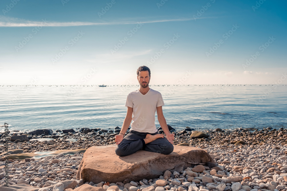 Attractive young man practicing yoga meditation and breathwork outdoors by the sea Attractive young man practicing yoga meditation and breathwork outdoors by the sea