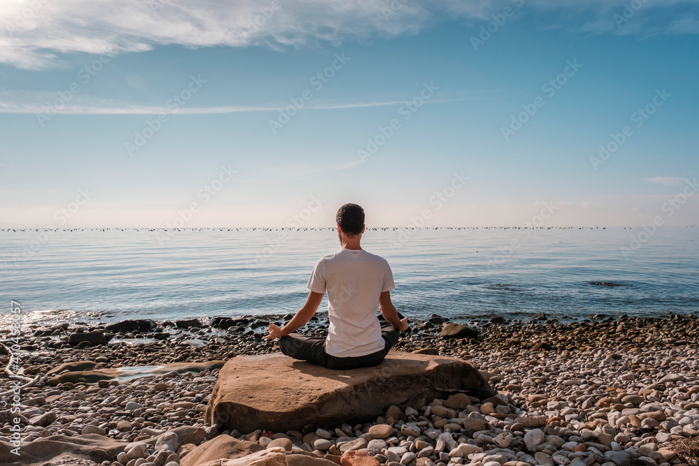 Attractive young man practicing yoga meditation and breathwork outdoors by the sea