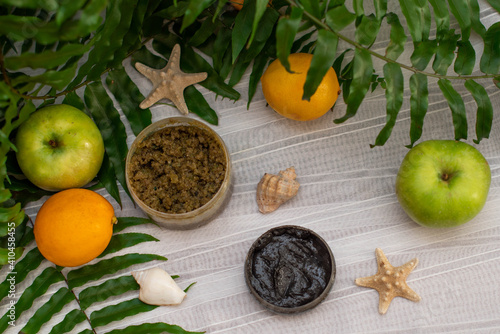 image of homemade cosmetics ingredients. aroma theme. Black mask, clay. organic cosmetics with extracts of herbs apples, lemons and oranges on white leaf green background