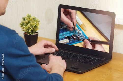 A man looks at a laptop online electronics repair courses. Soldering station with LED display, heating controller, with a soldering iron. Online learning concept.