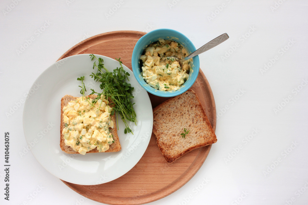 Egg salad sandwich with whole wheat toasted bread and microgreens on plate on white background. Healthy food concept
