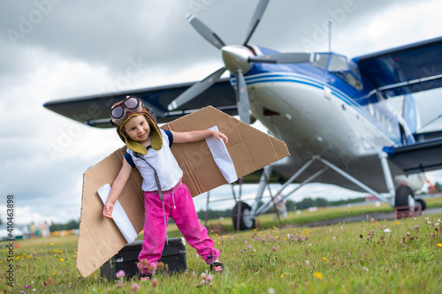 A cute little girl dressed in a cap and glasses of a pilot on the background of an airplane. The child dreams of becoming a pilot.