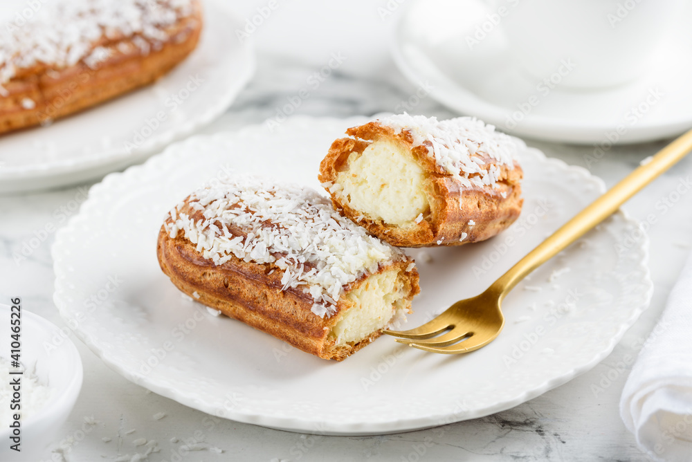 Coconut eclair on a white plate. Traditional french dessert. Cut eclair. Selective focus 