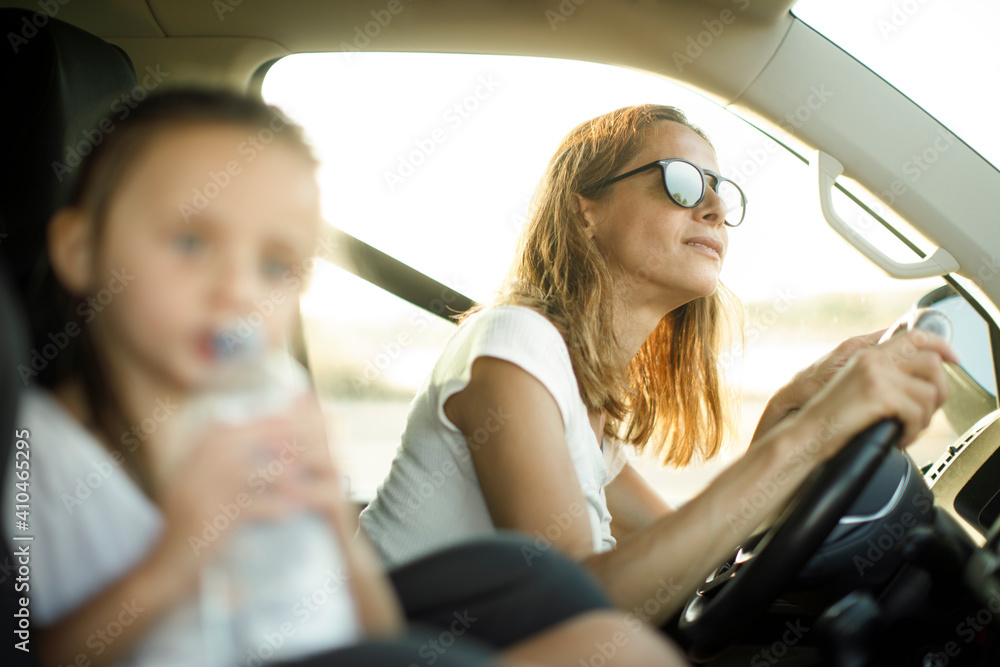 Donna al volante con maglietta bianca in contesto vacanziero viaggia con la figlia con espressioni sorridenti
