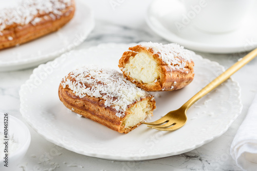 Coconut eclair on a white plate. Traditional french dessert. Cut eclair. Selective focus 