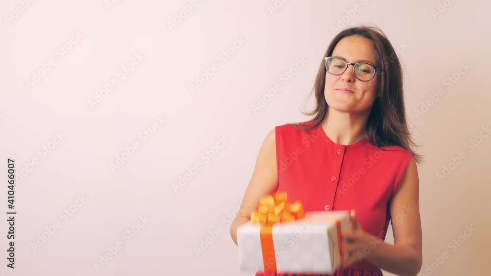 Happy girl throws the gift up and catches. Beautiful woman in glasses and in a red dress has fun: smiles and plays with a new donated box Happy girl throws the gift up and catches. Beautiful woman in glasses and in a red dress has fun: smiles and plays with a new donated box