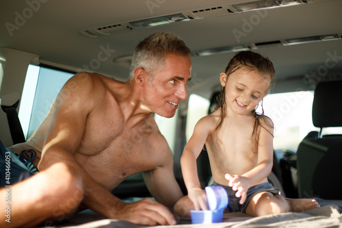 Uomo a torso nudo in contesto vacanziero gioca con la figlia seduti dentro il loro furgone photo