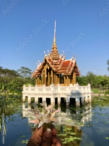 Flowers in a hand in front of a Thai temple building in a lake at King Rama IX Park in Bangkok, Thailand