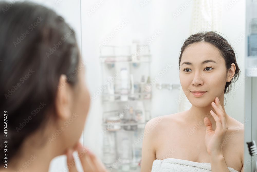 beautiful young Asian woman looks in the mirror after a shower in the
