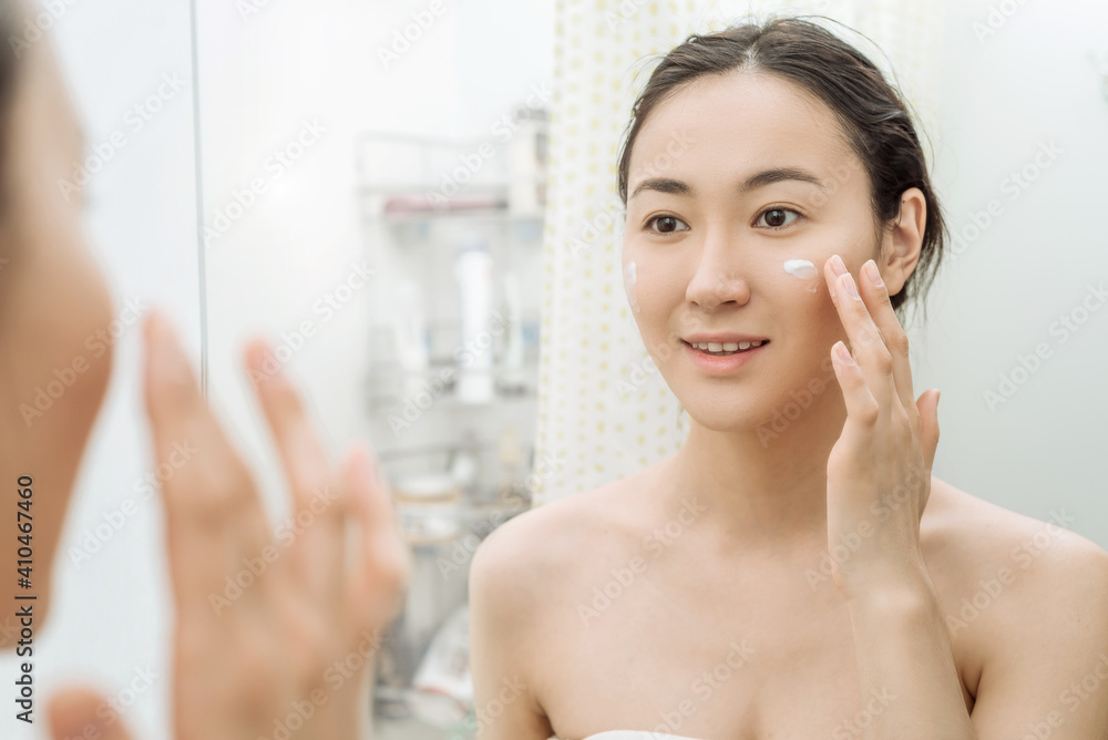 beautiful young Asian woman looks in the mirror after a shower in the