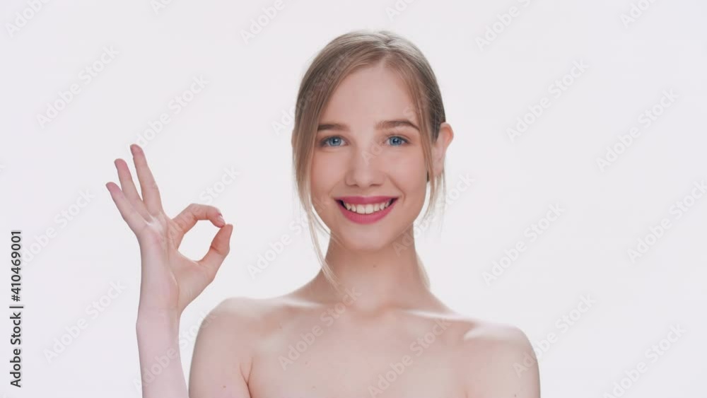 Close-up beauty portrait of young attractive blonde woman makes an ok gesture, looks at the camera and smiles widely Close-up beauty portrait of young attractive blonde woman makes an ok gesture, looks at the camera and smiles widely