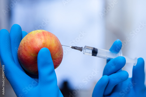 A biologist woman genetically modifies an apple for longer life. Female researcher or scientist using laboratory equipment for syringe in sterile clothing injects the vaccine GMO into the food.