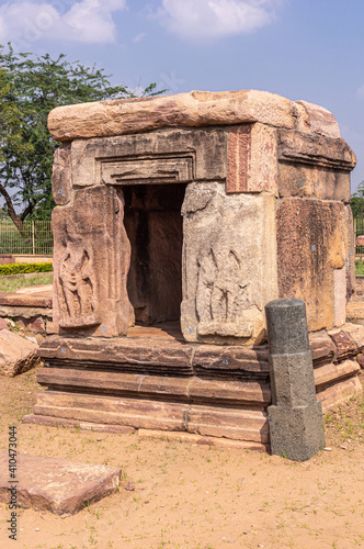 Bagalakote, Karnataka, India - November 7, 2013: Pattadakal temple complex. Closeup of cubical empty brown stone shrine with damaged sculptures under blue cloudscape and with green foliage. photo