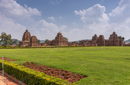 Bagalakote, Karnataka, India - November 7, 2013: Pattadakal temple complex. Wall of brown stone temple buildings set together under blue cloudscape and set in green park. photo