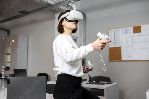 team of four creative engineers working with virtual reality, young woman testing VR glasses or goggles sitting in the office room photo