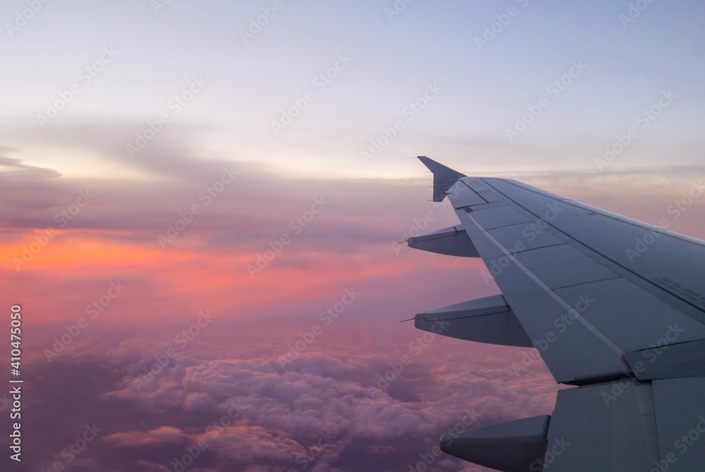 Fototapeta premium Wing of airplane above clouds in vivid colors sunset light.