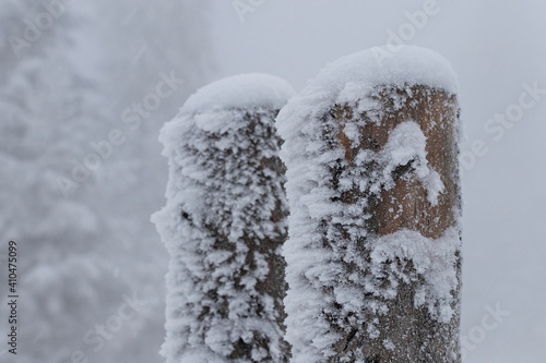 Frosted timber fence covered with fresh snow. Texture of ice on wood. Foggy weather in background