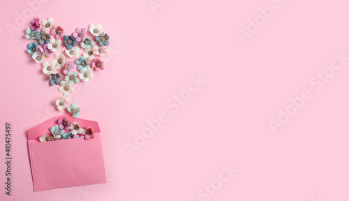 A heart shape of white, blue and pink flowers spills out of the envelope on a pink background. Valentine's Day, love, congratulations. Pastel colors. Top view, banner, space for text © Fotosova