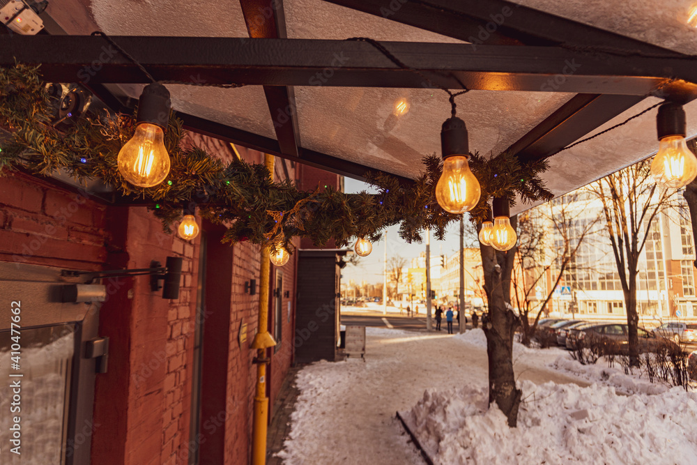 Cafe canopy is decorated with pine branches, Edison bulbs and shines with a warm yellow light
