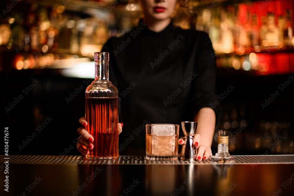 bottle of liquor and glass with cocktail and jigger on the bar