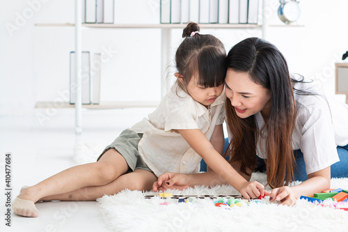 Young mother playing with her daughter in morning in bedroom. Mother and her child girl playing and hugging. Young Mother and daughter Having fun playing with colorful toys on carpet.