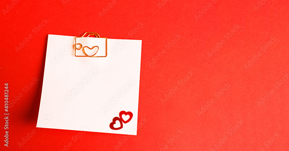 Square sheet for notes with a paper clip in shape of a letter and a heart. Decor of couples in love with hearts on a red background. Valentine's Day, message, greeting, declaration of love. Copy space