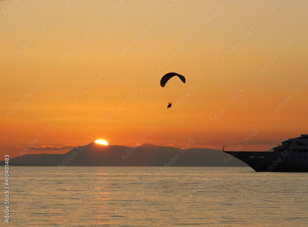 A powered paraglider, flying at sunset, in Glyfada, Greece A powered paraglider, flying at sunset, in Glyfada, Greece