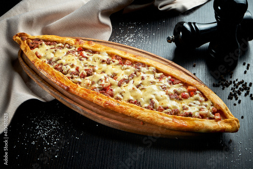 Turkish pide dish with slices of beef, tomatoes and cheddar cheese on black background photo