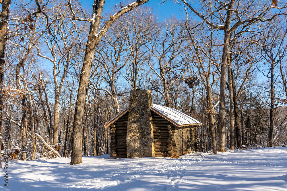 Log cabin in the snow covered woods with blue skies behind.