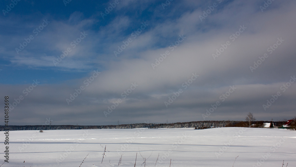 Suburbs of Grodno. Belarus. Winter landscape outside the city. A snow-covered field after a heavy snowfall, a forest and village houses in the distance against a blue sky with clouds.