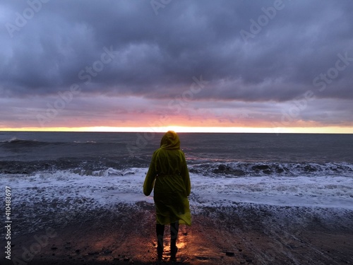 the person in a yellow raincoat looks at a beautiful sunset on the beach.